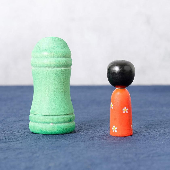 Kokeshi wooden doll with orange body and black head beside green bamboo-shaped wooden piece | Tsuchiyu, Fukushima
