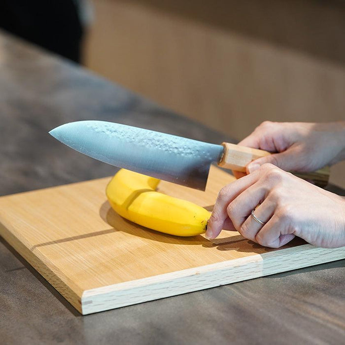 Santoku knife with hammered blade slicing a banana on a wooden cutting board | Sakai, Takahashi Kusu