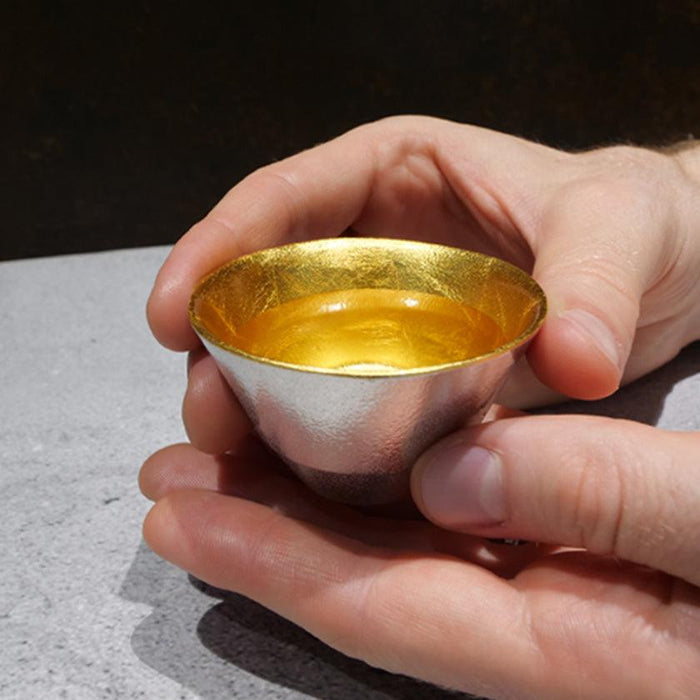 Tin sake cup with gold leaf interior held in two hands | Nousaku, Takaoka