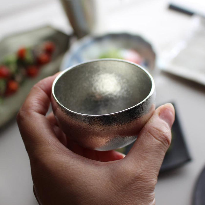 Hand holding a polished tin sake cup with hammered texture | Takaoka casting, Nousaku