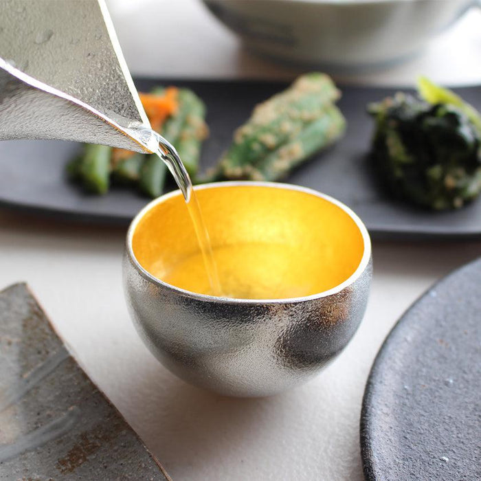Sake being poured into a tin and gold leaf sake cup | Takaoka casting, Nousaku